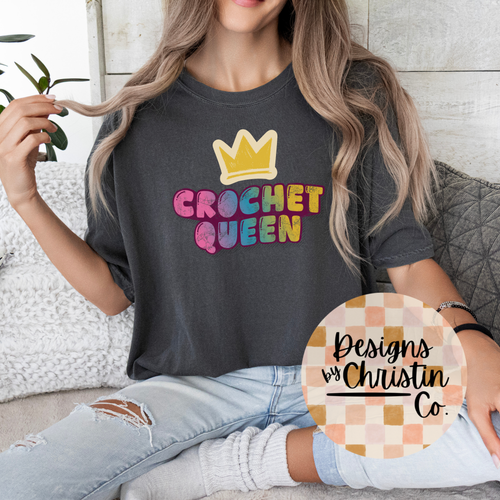 Person wearing a dark gray t-shirt with 'Crochet Queen' text and a crown graphic, sitting on a couch.