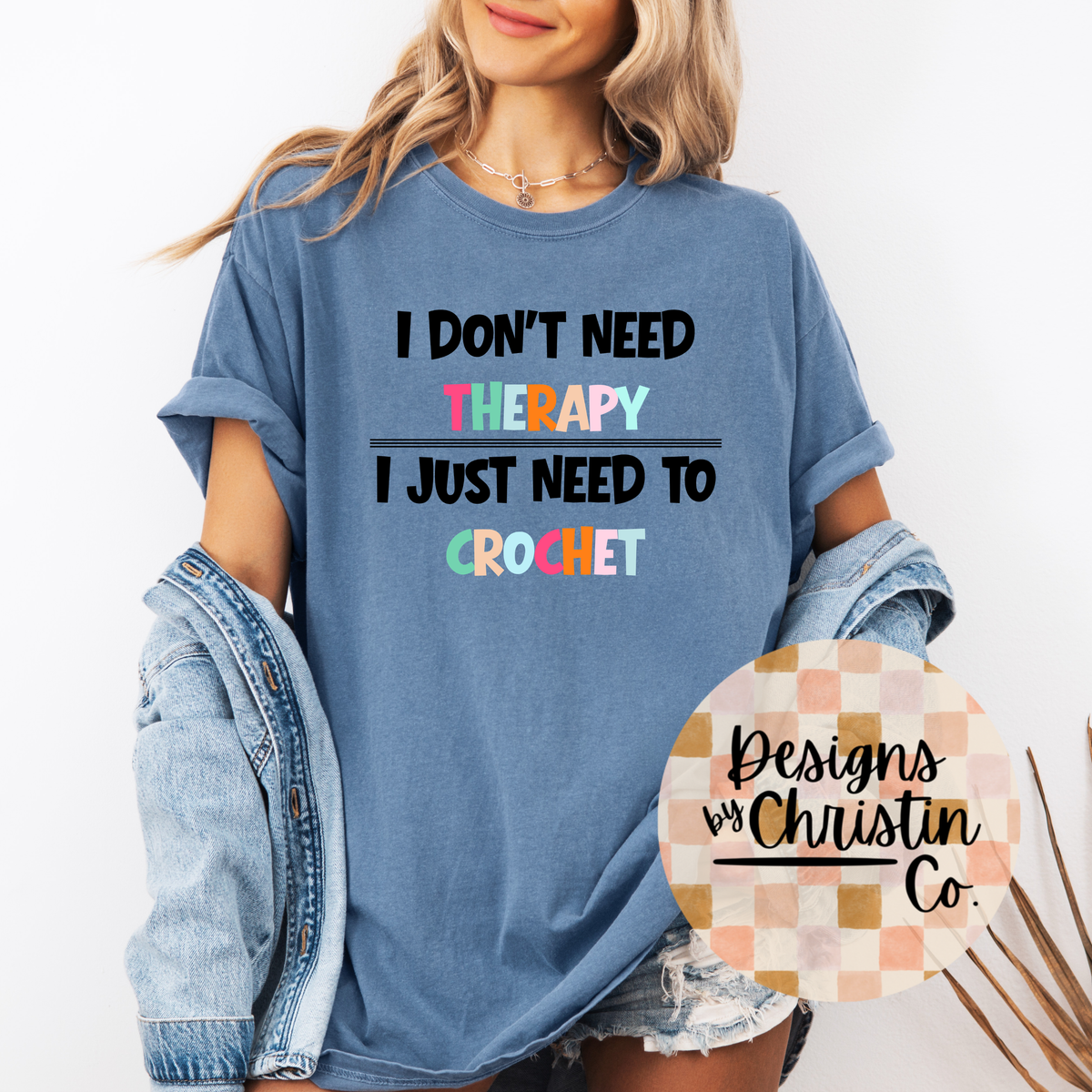Person wearing a blue t-shirt with colorful text 'I Don't Need Therapy I Just Need To Crochet' and a denim jacket.