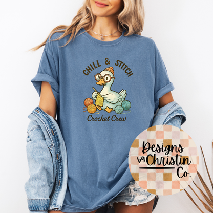 Person wearing a blue t-shirt with 'Chill & Stitch Crochet Crew' design, holding a denim jacket.