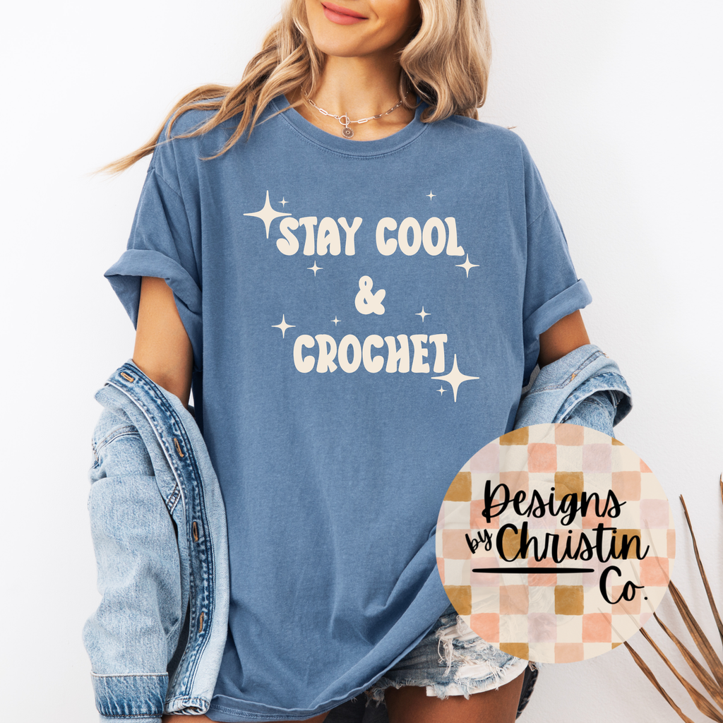Person wearing a blue t-shirt with 'Stay Cool & Crochet' text, holding a denim jacket.