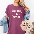Person wearing a purple t-shirt with 'Stay Cool & Crochet' text, standing against a white background.