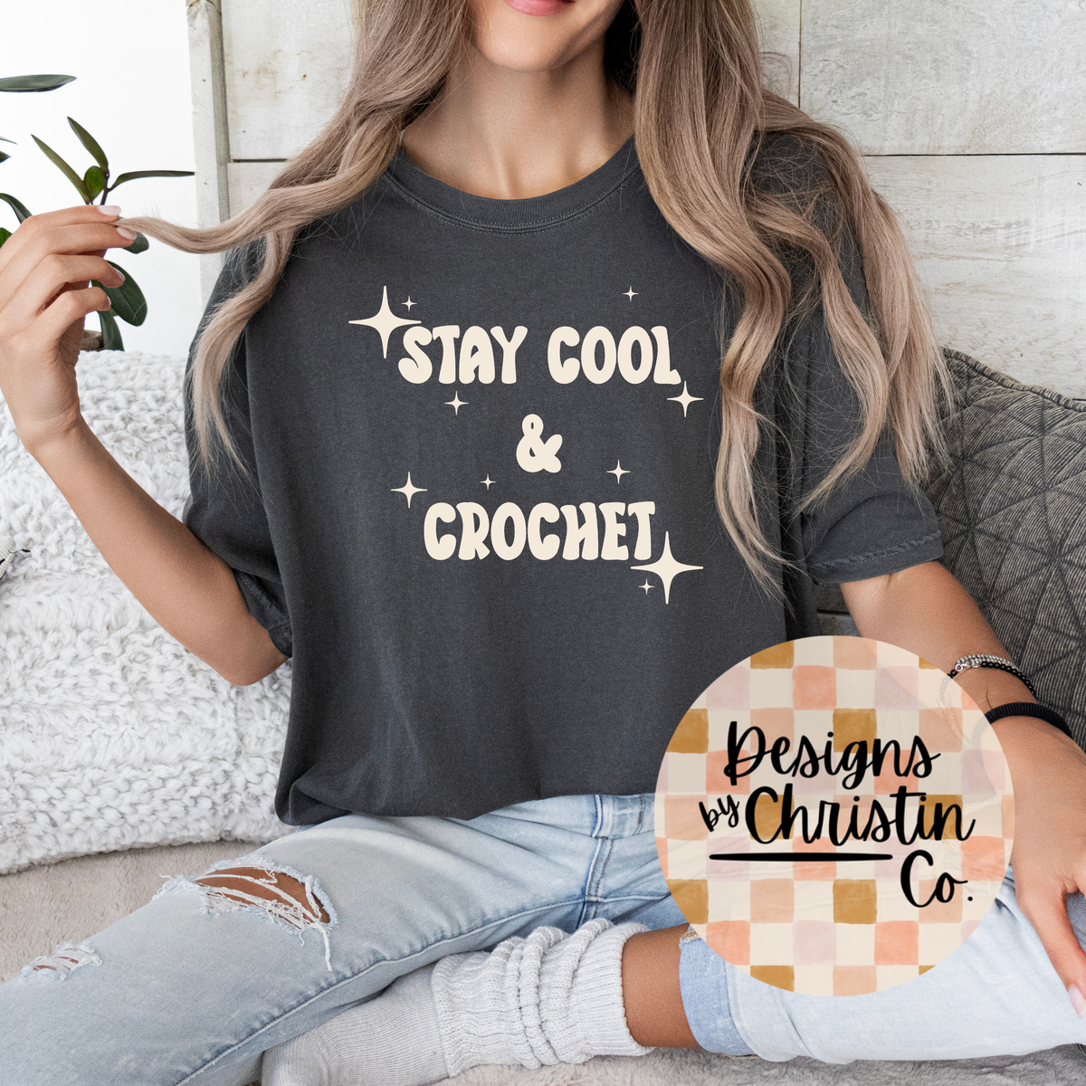 Person wearing a dark gray t-shirt with 'Stay Cool & Crochet' text, sitting on a couch.