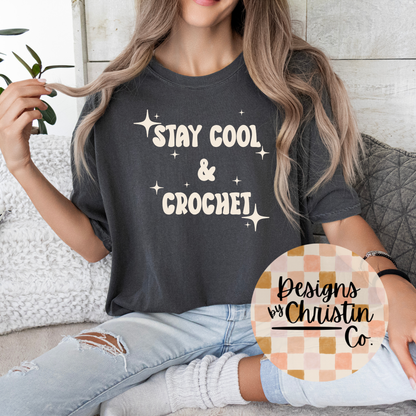 Person wearing a dark gray t-shirt with 'Stay Cool & Crochet' text, sitting on a couch.