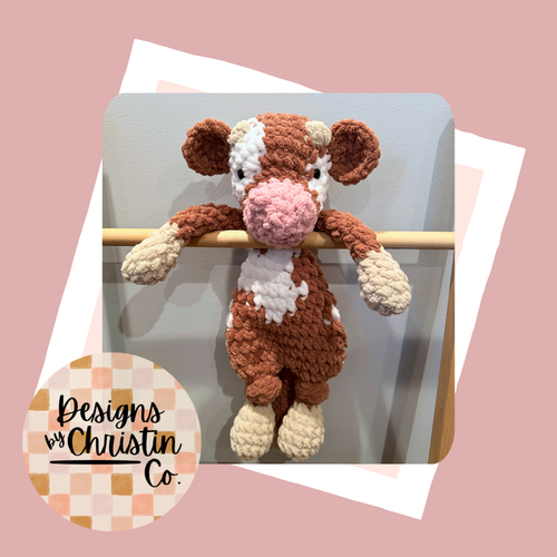 A crochet plush lovey resembling a cow with a brown and white color scheme.